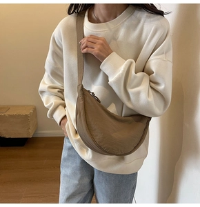 Brown nylon crescent bag shown worn as a crossbody on a model in a minimalist room