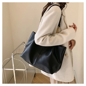 Detail view of large black tote bag with gold chain strap on model for styling scale