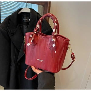 Close-up of red leather handbag with wavy texture, silk scarf handle, and gold hardware