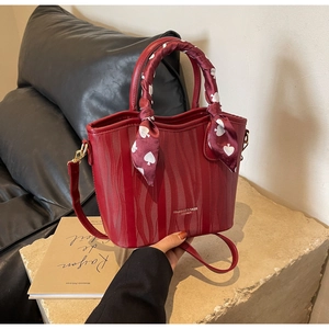 Detail of red ripple textured handbag with decorative silk scarf handle on leather sofa