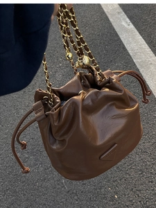 Detail of brown leather bucket bag with gold chain strap and drawstring closure