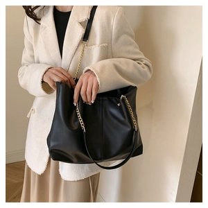 Close-up of a large black PU leather tote bag featuring gold chain and leather straps