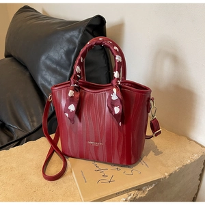 Macro view of burgundy water-ripple leather handbag with silk scarf detail and golden text