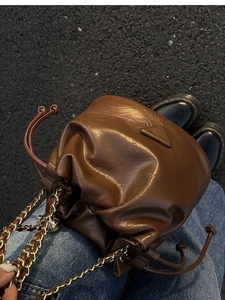 Close-up of brown leather bucket bag featuring a triangle logo and woven chain strap detail