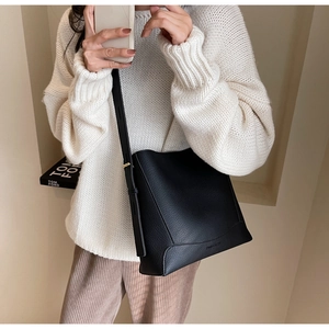 Detail of a black pebbled leather bucket bag with adjustable strap on a neutral sweater