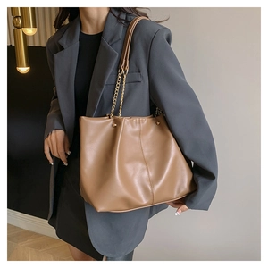 Brown leather tote bag with gold chain strap shown on model in a modern office setting