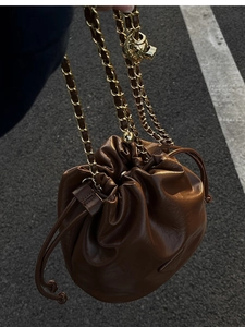 Close-up of brown drawstring bucket bag featuring a gold skull charm and chain strap