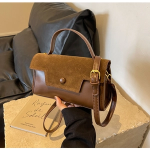 Detail of a brown leather and suede crossbody bag featuring gold-tone hardware and buckles
