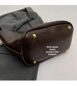 Close-up of four golden wear-resistant rivets on the bottom of a dark brown bucket bag