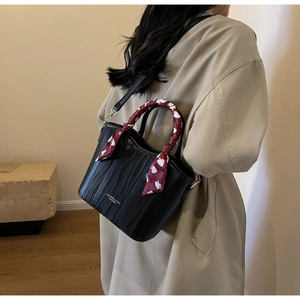 Detail of black leather handbag with vertical textures and heart pattern silk scarf handle