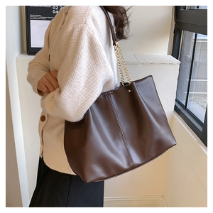 Detailed side view of a large brown tote bag with elegant gold chain strap for daily commute