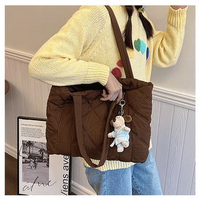 Detail of a brown quilted nylon tote bag with a cute plush charm on a casual outfit