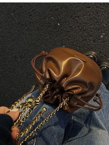 Detail of a brown leather drawstring bucket bag with gold chain and metal logo plate