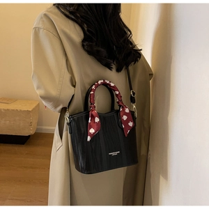 Detail of black wave-patterned leather handbag with decorative red heart-print silk scarf