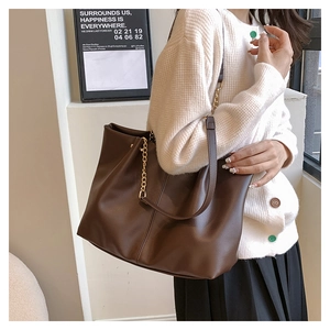 Detail of dark brown leather tote bag with gold chain strap on a stylish model