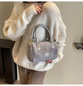 Détail du sac oreiller en peluche grise avec poignées en cuir et logo métallique doré