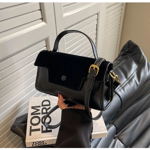 Detail of black structured handbag featuring velvet flap and gold-tone metal hardware