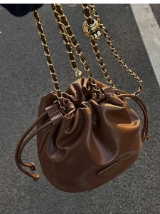 Close-up of brown leather bucket bag featuring a gold chain strap and drawstring closure