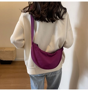 Close-up of a purple crescent nylon bag worn by a model in a minimalist setting