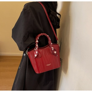 Detail of red textured bucket bag with decorative heart print silk scarf on handle
