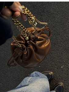 Detail of a dark brown pleated bucket bag with a chunky gold chain strap and drawstring