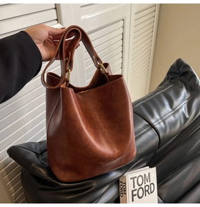 Close-up of vintage brown leather bucket bag with embossed fashion text and metal rings