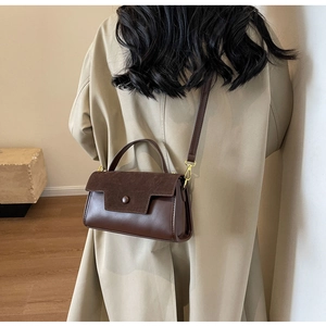 Detail of dark brown crossbody bag featuring mixed texture suede flap and gold buckle hardware