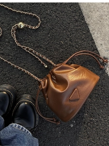 Close-up of brown leather bucket bag featuring drawstring closure and gold chain strap