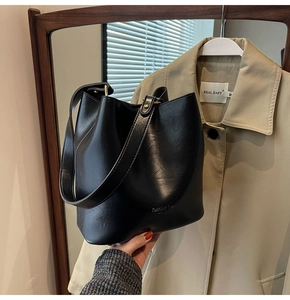 Detail of a black glossy PU leather bucket bag featuring a fashion bag inscription and strap