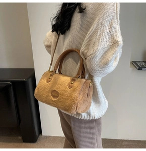 Détail du sac polochon en peluche camel avec poignée en cuir et emblème gravé