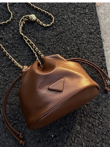Detail of a brown drawstring bucket bag featuring a gold chain strap and triangle patch
