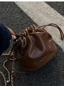 Close-up of dark brown wrinkled leather bucket bag with gold chain strap on street