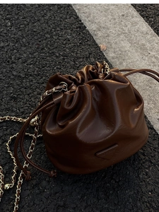 Detailed close-up of brown oiled leather bucket bag with chain strap and triangle logo