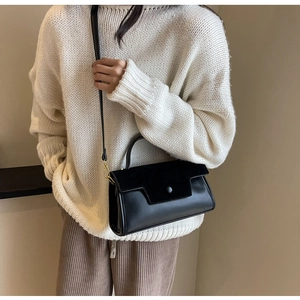 Detail of black leather crossbody square bag with gold hardware on a model