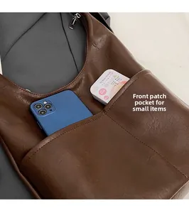 Dettaglio della tasca frontale di una borsa a secchiello marrone con smartphone