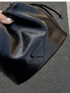 Detail of glossy black drawstring bucket bag featuring a wrinkled leather texture and logo