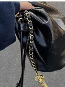 Close-up of black glossy leather bucket bag with gold chain strap and metal accents