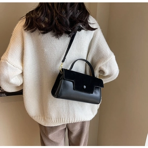 Detail of black crossbody bag with mixed textures styled on white knit sweater