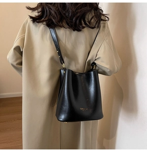 Detail of a vintage black leather bucket bag with gold lettering on a khaki trench coat