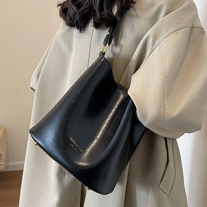 Classic black leather bucket bag with gold lettering shown on shoulder by model