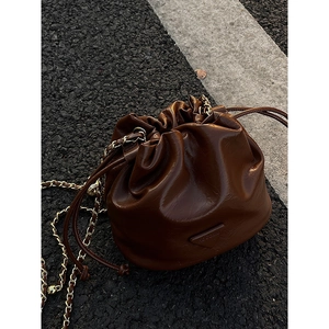 Retro brown oil-wax leather bucket bag with gold chain strap on asphalt background