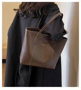 Detail view of large brown leather tote bag with white contrast stitching on model