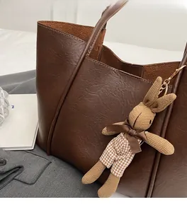 Detail of dark brown leather tote bag with a cute knit rabbit charm and textured finish