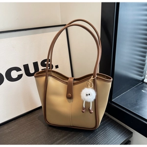 Dettaglio della borsa tote beige con bordo marrone e ciondolo in peluche bianco
