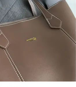 Detail of dark brown leather tote with contrasting white stitching and gold logo