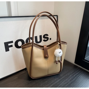 Dettaglio della borsa tote beige con bordo marrone e simpatico ciondolo mostro di peluche