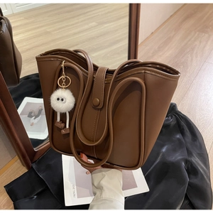Dettaglio di una borsa tote in pelle marrone con bordo circolare e ciondolo in peluche bianco