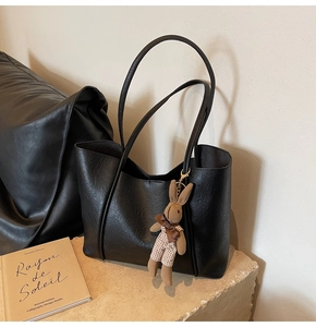 Close-up of black leather tote bag with fine litchi texture and cute plush bunny charm