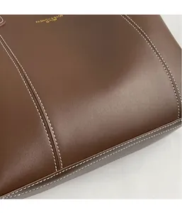 Detail of dark brown leather tote featuring contrast white stitching and gold embossed logo