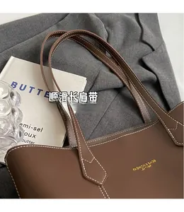 Detailed shot of dark brown leather tote featuring white stitching and gold lettering